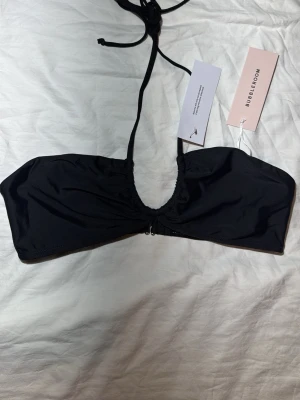 Svart bandeau bikiniöverdel Bubbleroom - Stilren svart bandeau bikiniöverdel från Bubbleroom med smala knytband i nacken och en liten dragkedja framtill. Tillverkad i ett mjukt och stretchigt material som sitter bekvämt. Perfekt för dig som vill ha en enkel men trendig look på stranden.