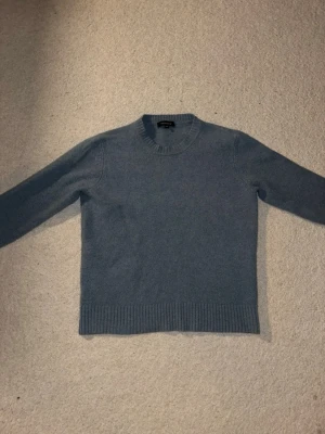 Blå stickad tröja från Paul & Friends - Mysig blå stickad tröja från Paul & Friends med rund halsringning och ribbade muddar vid ärmslut och nederkant. Enkel och stilren design som passar perfekt till lager på lager under kyliga dagar. Den är liten i storleken då den krympt. Skriv vid funderingar!