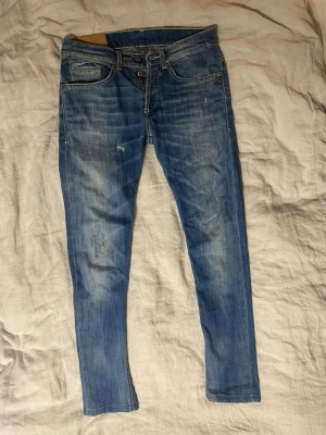 Dondup George - Säljer ett par blå Dondup jeans i modell George med lätt slitna detaljer och klassisk femficksdesign. Jeansen har låg midja och smal passform hela vägen ner. Perfekta till en avslappnad look och tillverkade i mjukt denimtyg.