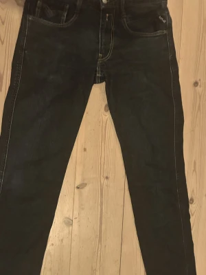 Svarta Replay jeans - Snygga svarta jeans från Replay med klassisk femficksdesign och slim ben. Jeansen har diskreta sömmar och logga på bakfickan. Perfekta för dig som gillar en stilren look och vill ha ett par jeans som funkar till det mesta.