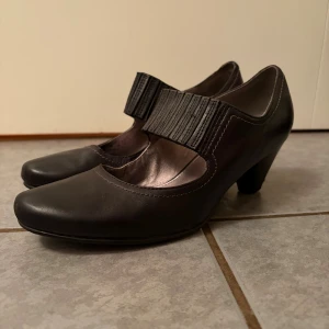 Svarta pumps från ECCO med klack - Stilrena svarta pumps från ECCO med rund tå och bred resårdetalj över foten. Skorna har en bekväm klack och är tillverkade i skinn. Perfekta för dig som vill ha både stil och komfort. Syns att den är smått använd inuti, inget slitage syns på utsidan. 