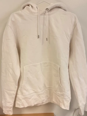 J.Lindeberg hoodie - Säljer en stilren ljusbeige hoodie från J.Lindeberg med broderad logga på bröstet. Hoodien har en klassisk huva med dragsnören och en stor magficka framtill. Den är vi väldigt fint skick. 
