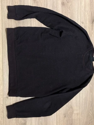 Svart sweatshirt från Smog - En stilren svart sweatshirt från Smog i slim fit-modell. Tröjan har rund halsringning, långa ärmar och ribbade muddar vid ärmslut och nederkant. Perfekt för en enkel och clean look. Sitter som storlek M