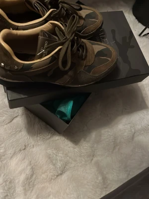 Valentino Rockrunner sneakers camouflage - Snygga Valentino Rockrunner sneakers med camouflage-mönster i grönt, brunt och beige. Skorna har snörning, detaljer i mocka och skinn samt nitar på hälen. Perfekta för dig som vill sticka ut med en cool streetstyle.