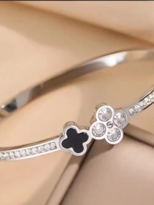 Silverfärgat armband med blommor - Snyggt armband i guld pläterad med två blommor framtill, en i svart emalj och en dekorerad med gnistrande stenar. Armbandet har en stilren, smal design med små infattade stenar längs bandet. Perfekt accessoar för dig som gillar elegant och modern stil.