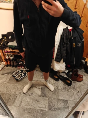 Mörkblå hoodie från Polo Ralph Lauren - Snygg mörkblå hoodie från Polo Ralph Lauren med dragkedja, huva och två fickor framtill. Klassisk röd logga broderad på bröstet och vita detaljer i snöret. Perfekt för en avslappnad och stilren look.