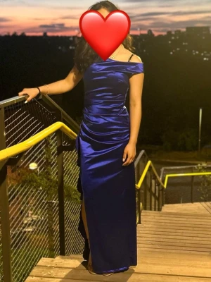 Marinblå axelbandslös långklänning/ Balklänning  - Säljer en elegant marinblå långklänning i glansigt material med offshoulder-design och slits framtill. Klänningen har figurnära passform och vacker drapering längs sidorna. Perfekt för dig som vill sticka ut på bal eller fest. Jag är 158 cm, klack skon var 4 cm. 