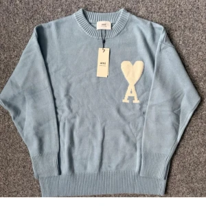  Ami Sweater baby blue - Snygg ljusblå stickad tröja från Ami med rund halsringning och ribbade muddar. På bröstet finns ett vitt hjärta och bokstaven A som ger en unik touch. Perfekt för dig som gillar stilrena och trendiga plagg.