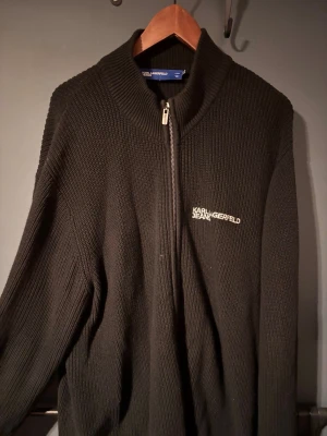 Svart stickad kofta Karl Lagerfeld - Säljer en svart, ribbstickad kofta från Karl Lagerfeld Jeans i storlek Large. Koftan har hel dragkedja framtill, hög krage och diskret logga broderad på bröstet.