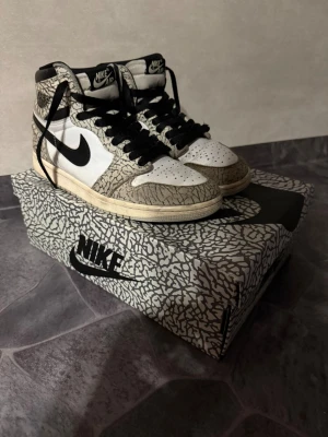 Nike Air Jordan 1  - Säljer ett par Nike Air Jordan 1 High med ikoniskt elephant print i grått och svart, vita paneler och svarta detaljer. Skorna har svart swoosh, svarta skosnören och hög siluett. Kommer med originalkartong i matchande mönster. Perfekta för dig som gillar unika sneakers. Du kanske ska köpa ett par nya snören till den för en av dem är lite sliten. Kvitto finns!!! Priset kan diskuteras dem kostade mig 2000kr 