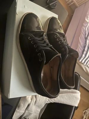 Svarta sneakers med lackad tå - Snygga svarta sneakers med rund tå och lackad tådel. Skorna har snörning och en vit sula som kontrast. Materialet är en mix av textil och lackdetaljer vilket ger en cool och modern look. Tar gärna byten