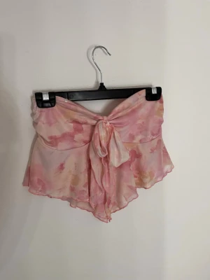 Rosa bandeau topp med knyt - Säljer en superfin bandeau topp i ljusrosa och persikofärgade toner med omlott och knyt framtill. Toppen är ärmlös och har ett flowy, lätt material. Perfekt för sommaren. Aldrig använd.