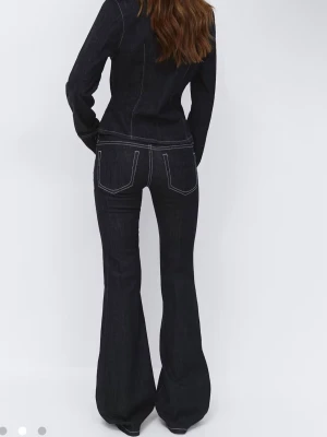 Mörkblå bootcut jeans med kontrastsömmar - Snygga mörkblå bootcut jeans med vita kontrastsömmar och klassisk femficksdesign. Jeansen har låg midja och är tillverkade i ett stretchigt denimtyg som ger en bekväm passform. Perfekta för dig som vill ha en retroinspirerad look.