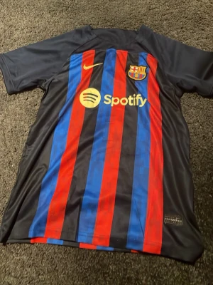 FC Barcelona matchtröja Nike - Säljer en FC Barcelona matchtröja från Nike med klassiska blå och röda vertikala ränder. Tröjan har klubbmärke, Nike-logga och Spotify som sponsor framtill samt UNHCR-logga på ryggen. Tillverkad i lätt och ventilerande material, perfekt för fotbollsträning eller match.