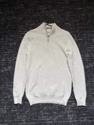 stickad tröja med halvzip - Snygg vit/beige stickad tröja från John henric med halv dragkedja och hög krage. Tröjan har diskret strukturmönster, ribbade muddar vid ärmslut och nederkant samt en stilren look som passar till det mesta.