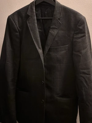 Svart rutig kavaj från Tiger of Sweden man storlek 148 - Snygg svart kavaj från Tiger of Sweden med diskret rutigt mönster. Klassisk modell med två knappar framtill, bröstficka och två sidofickor. Tunn fodring. Mörkgråblå i färgen.