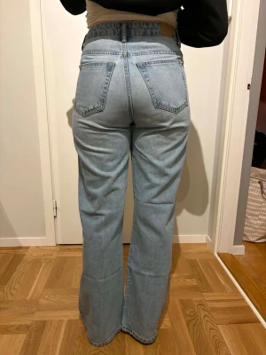 Ljusblå high waist bootcut jeans - Säljer ett par ljusblå jeans med hög midja och bootcut passform. Jeansen har slitna detaljer på båda benen framtill och klassiska fem fickor. Tillverkade i bomull med en skön jeanskänsla. Perfekta för en avslappnad och trendig look.