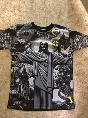 Grafisk Neymar Jr. Brasilien T-shirt - Unik t-shirt med grafiskt svartvitt tryck av Kristusstatyn och brasilianska motiv. Neymar Jr. och nummer 10 på ryggen. Korta ärmar, rund hals och detaljer i gult och grönt. Perfekt för dig som älskar fotboll och streetstyle.