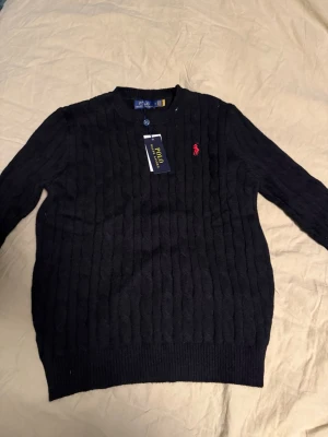 Svarta  kabelstickad tröja Polo Ralph Lauren - Säljer Ralph Lauren-tröjor eftersom jag har många hemma och inte vet vad jag ska göra med dem. Därför har jag valt att sälja dem billigt. För dig som vill ha en tröja av bra kvalitet. Vill sälja snabbt. Tröjorna är oanvända. Storlek M