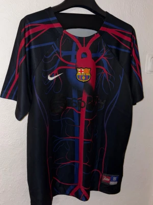 Barcelona Nike matchtröja Spotify - Säljer en officiell FC Barcelona matchtröja från Nike med Spotify-logga. Tröjan är svart med blå och röda detaljer i ett unikt ådringsmönster, klubbmärke på bröstet och Nike swoosh. Tillverkad i lätt och ventilerande material, perfekt för fotboll eller träning.