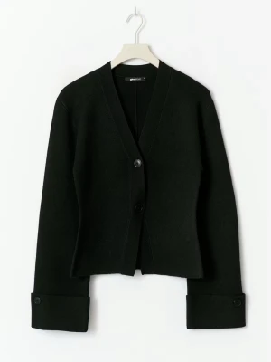 Svart cardigan från gina tricot - Stilren svart cardigan från Gina Tricot med två knappar framtill och breda muddar med knappdetalj vid ärmsluten. Tillverkad i mjukt stickat material och har en rak, något boxig passform. Perfekt för lager på lager och enkel att matcha.