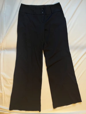 Svarta vida kostymbyxor - Vida, medelhög midja. Storlek: 36, längd skrev till midja: 24 cm, total längd: 98 cm, innerbenslängd:  76 cm, midjemått: 36.5 cm, vidd på benet (längst ned) 28 cm. Byxorna är i bra skick förutom längst ned där de har fått en ny, ganska ful söm (syns på bilder 4-5) skulle behövas sys upp nån cm.