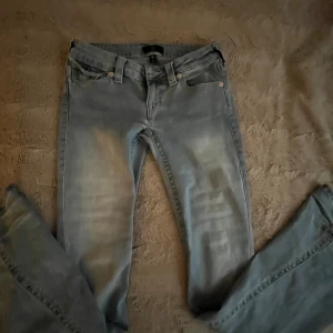True Religion Joey Low Rise Flare Jeans - Ljusblå jeans från True Religion i storlek W25, modell Joey Low Rise Flare. Snygg bootcut med mycket låg midja och detaljer på fickorna. De är knappt använda men jeansen är lite slitna som man kan se på en av bilderna, men det är längst ner så det syns inte när man har på sig dom🩷