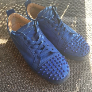 Blå Louboutin med nitar och mocka - Unika blå sneakers i mocka från Christian Louboutin med coola nitar över tån och klassisk röd sula. Skorna har snörning, svarta sulor och beige innersida. Perfekt för dig som vill sticka ut med en edgy och lyxig stil. Pris kan diskuteras och kan även gå med på byte