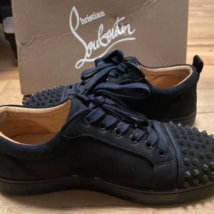 Christian Louboutin svarta sneakers med nitar - marinblå sneakers från Christian Louboutin med coola svarta nitar på tån och klassisk röd sula. Skorna har snörning, rund tå och är tillverkade i skinn. Snygg och edgy design som sticker ut, perfekt för dig som vill ha något extra.
