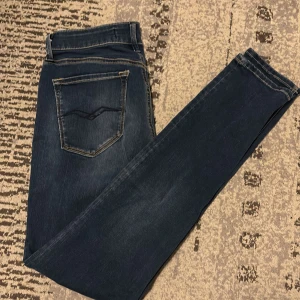 Replay jeans i mörkblå denim - Säljer ett par snygga Replay jeans i mörkblå tvätt med klassiska kontrastsömmar och diskret Replay-logga vid fickan. Modellen har smal passform och raka ben, perfekt till sneakers eller boots. Materialet är mjukt och stretchigt jeans för extra komfort.
