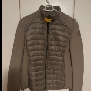 Beige pufferjacka från Parajumpers S - HELT NY Snygg beige pufferjacka från Parajumpers med quiltad front, släta ärmar och klassisk gul detalj vid kragen. Jackan har dragkedja framtill, diskret logga på ärmen och är perfekt för kyliga dagar. Materialet är polyester och syntet.