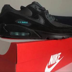 Nike Air Max 90 Svart/Turkos US8 - Säljer ett par Nike Air Max 90 i svart med turkosa detaljer. Skorna har en klassisk siluett med mesh och mocka på ovandelen, samt den ikoniska Air Max-dämpningen i sulan. Snygga snörade sneakers som passar perfekt till streetwear-stilen.
