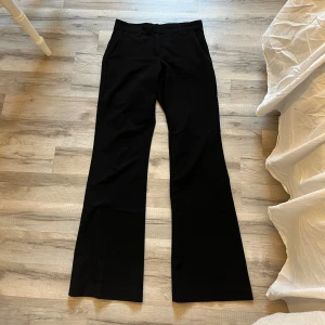 Svarta bootcut kostymbyxor - Svarta kostymbyxor med bootcut-snitt och klassiska fickor framtill. Byxorna har hällor för bälte och en stilren, tidlös look som passar till många olika outfits. Perfekta för dig som gillar en lite vidare passform nertill.