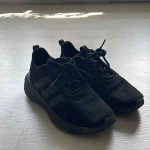 Svarta Adidas sneakers med mesh - Säljer ett par helsvarta Adidas sneakers med klassiska tre ränder på sidan. Skorna har ovandel i mesh för bra andningsförmåga, snörning och en rejäl platt sula. Perfekta för dig som gillar stilrena och sportiga skor.