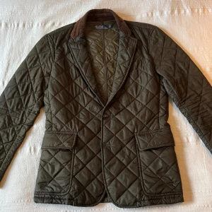 Quiltad Ralph Lauren Jacka - Quiltad jacka från Polo Ralph Lauren i storlek S. Jackan är mörkgrön med snygga mocka och manchester detaljer som passar perfekt till höst och vinter! Modellen är 173 cm 70 kg. Hör av er vid frågor, pris går att diskutera. 