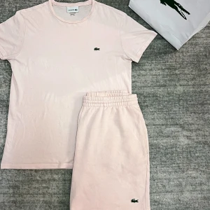 Ljusrosa t shirt och shorts från Lacoste - Säljer ljusrosa t shirt och shorts från Lacoste med elastisk midja och klassisk krokodil-logga broderad framtill. Mjukt bomullsmaterial som är riktigt skönt och perfekt för varma dagar. Enkel och clean design som passar till allt.