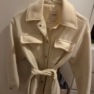 Kappa - Stilren beige overshirt från Koton med stora bröstfickor, knappar framtill och bälte i midjan. Jackan har klassisk krage och är långärmad, perfekt för lager-på-lager. Materialet är mjukt och ger en clean look.