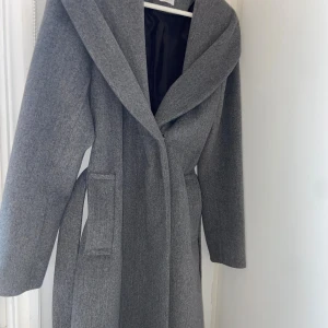 Grå kappa från Primark med bälte - Snygg grå kappa från Primark med bred krage och knytskärp i midjan. Lång modell med raka ärmar och stora fickor framtill. Perfekt för dig som gillar stilrena och klassiska plagg med en modern touch nj i höst😍❤️