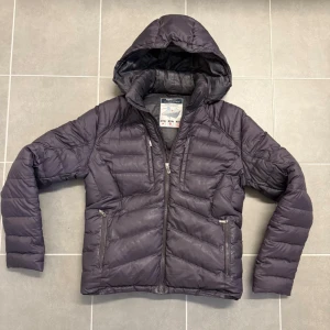 Mörkblå dunjacka från Zegna - Mörkblå dunjacka från Zegna med huva och dragkedja framtill. Jackan är quiltad och har två sidofickor med dragkedja. Ultralätt och varm med hög isolering, perfekt för kalla dagar. Klassisk passform och stilren look.