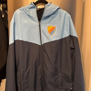 Djurgården jacka blå S - Säljer en snygg tvåfärgad fleecefodrad jacka från Djurgårdens IF i ljusblått och mörkblått. Jackan har huva med snörning, dragkedja framtill och broderat DIF-märke på bröstet. 