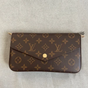Louis Vuitton Monogram axelväska - Snygg axelväska från Louis Vuitton i klassiskt monogrammönster. Väskan är brun med guldiga detaljer och kedja, tillverkad i skinn. Kommer med matchande plånbok och innerficka, perfekt för att hålla ordning på dina grejer.