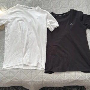 2-pack Calvin Klein t-shirts svart & vit - Två stilrena t-shirts från Calvin Klein i svart och vitt. Båda har klassisk passform, rund hals och diskret CK-logo på bröstet. Tillverkade i mjuk bomull som är skön mot huden. Perfekta för en clean och enkel look. ⚠️nacken är lite utstretchad på de ⚠️