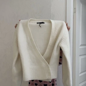 Vit kofta med v-ringning från Bik Bok - Superfin vit kofta från Bik Bok med djup v-ringning och tre knappar framtill. Den är stickad och har långa ärmar samt ribbade muddar vid nederkanten. I mycket bra skick då jag bara använt den 3 gånger!!
