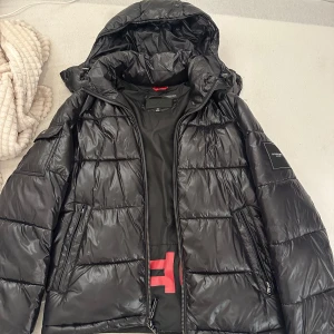 Svart pufferjacka från Michael Kors - Snygg svart pufferjacka från Michael Kors med avtagbar huva, stora fickor och dragkedja. Insidan har röd logga och detaljer. Har bara använts några få gånger🫶🏼Funkar även som storlek S-M!!
