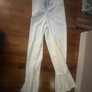 Vita kostymbyxor från Promthong M - Snygga vita kostymbyxor från Promthong i storlek M. Byxorna har hög midja och raka ben med klassisk passform. Perfekta för en clean och stilren look. Materialet känns mjukt och har en lätt glansig finish.