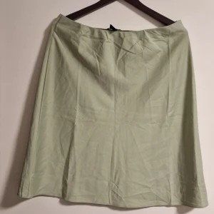 Ljusgrön kjol från Lindex - Enkel och stilren ljusgrön kjol från Lindex i A-linjeformad modell. Kjolen är knälång och har en mjuk, slät yta utan mönster eller detaljer. Perfekt för dig som gillar minimalistisk stil.