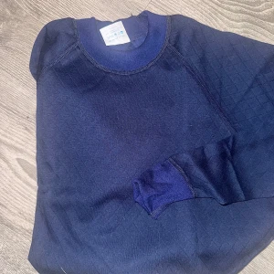 Mörkblå underställ från Fristads M - Mörkblå långärmad underställ från Fristads i funktionsmaterial, perfekt för lager-på-lager. Tillverkad i 58% polyester och 42% bomull med diskret rutmönster. Klassisk rund halsringning och mjuk och varm känsla. Bra inför kalla vintern. Unisex. 