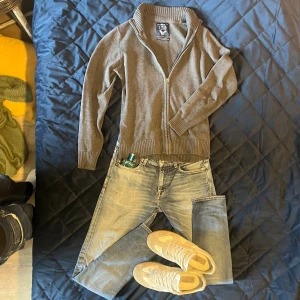 Grå kofta helzip från JFK - Grå kofta från J.F.K i 100% pima bomull. Tröjan har ribbade muddar, hög krage och hel dragkedja framtill. Perfekt för lager-på-lager och funkar snyggt till jeans. Enkel och stilren design som passar till många outfits.