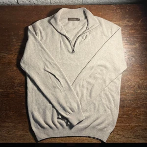 Beige half zip-tröja Oscar Jacobson - 7% Kashmir. Snygg beige stickad tröja från Oscar Jacobson med half zip-dragkedja och hög krage. Tröjan är i mjuk ull och har långärmad passform. Perfekt för lager-på-lager och stilrena outfits.