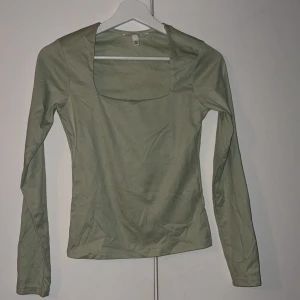 Ljusgrön långärmad topp med fyrkantig ringning - Snygg ljusgrön långärmad topp med fyrkantig ringning. Modellen är figurnära och passar perfekt till jeans eller kjol. Tillverkad i mjukt bomullsmaterial som känns skönt mot huden. Enkel och stilren design som är lätt att matcha.